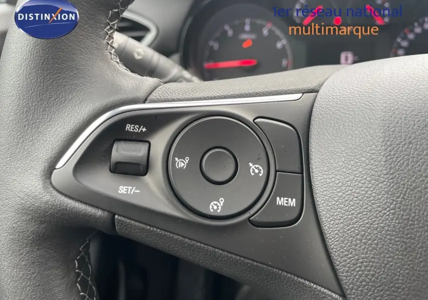 Gros plan sur les commandes au volant du Opel Crossland gris minéral 2022, avec tableau de bord flou en arrière-plan.