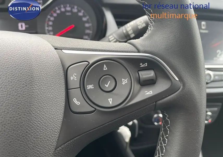 Gros plan sur les commandes du volant en cuir noir de l'Opel Crossland gris minéral, avec tableau de bord flou en arrière-plan.