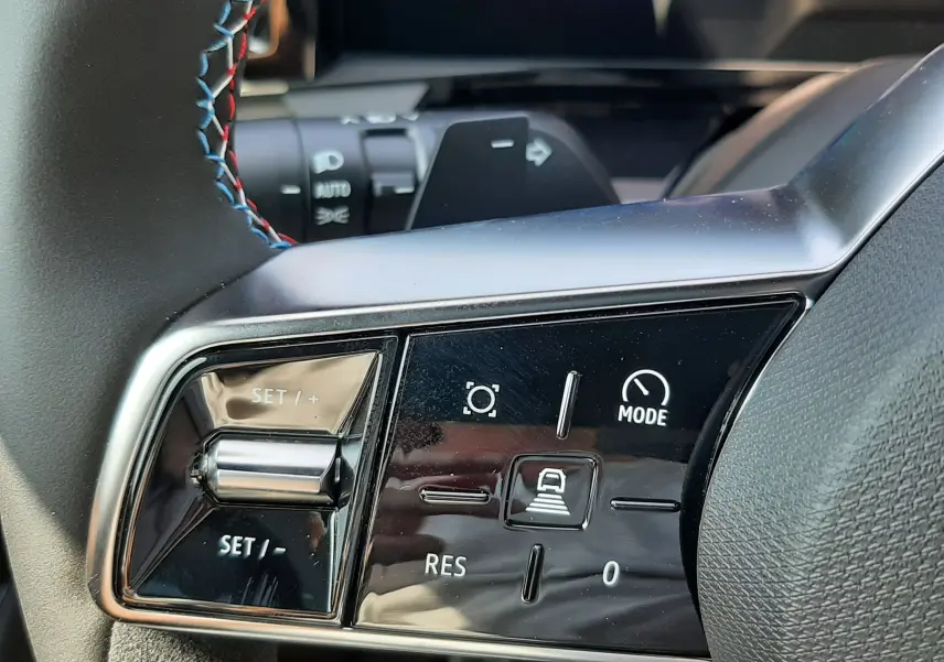 Gros plan sur les commandes au volant gauche du Renault Espace VI gris schiste, avec surpiqûres tricolores visibles.