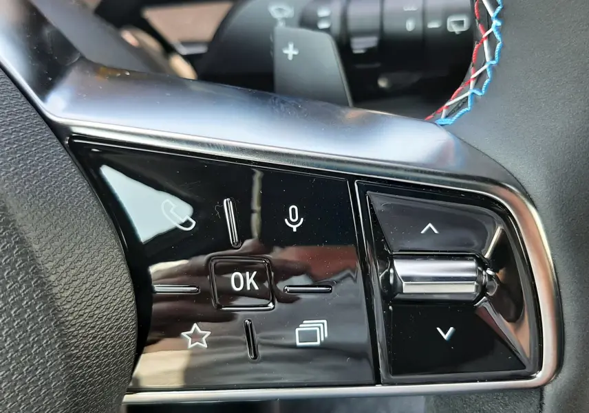 Gros plan sur les commandes au volant côté gauche du Renault Espace VI gris schiste, avec surpiqûres tricolores visibles.