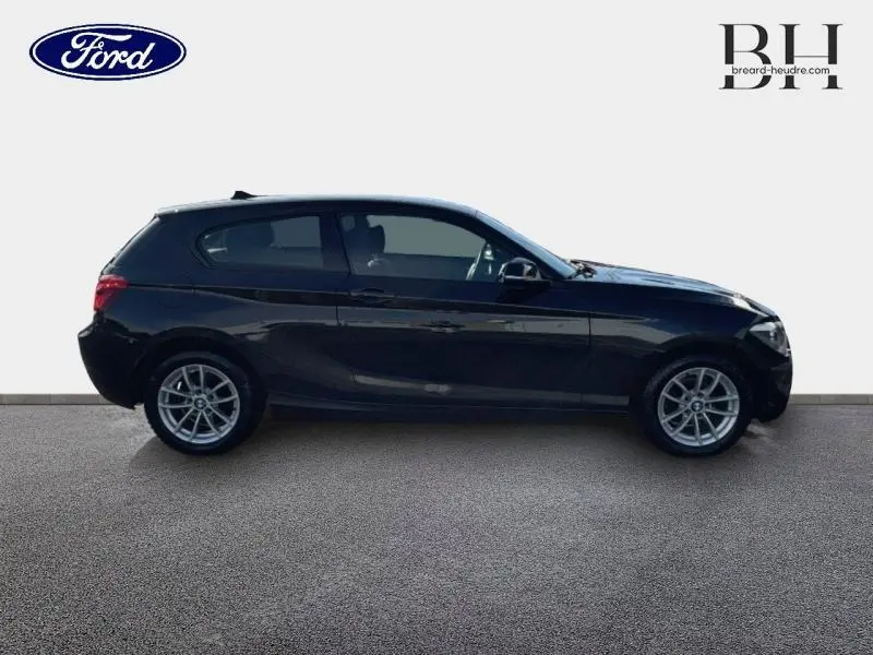 Profil côté gauche d'une BMW Série 1 114i Lounge noire, avec jantes alliage et vitres teintées.