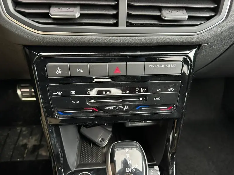 Vue rapprochée du tableau de bord et de la console centrale du Volkswagen T-Cross 2025 Gris Ascot avec commandes climatisation et boîte auto.