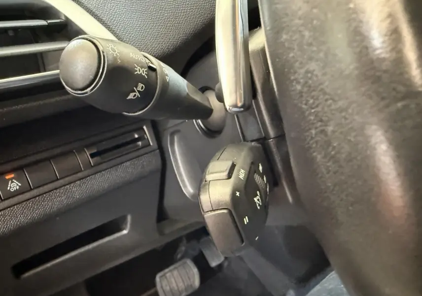 Gros plan sur la commande multifonction noire au volant d’un Peugeot 3008 bleu, avec tableau de bord partiel visible.