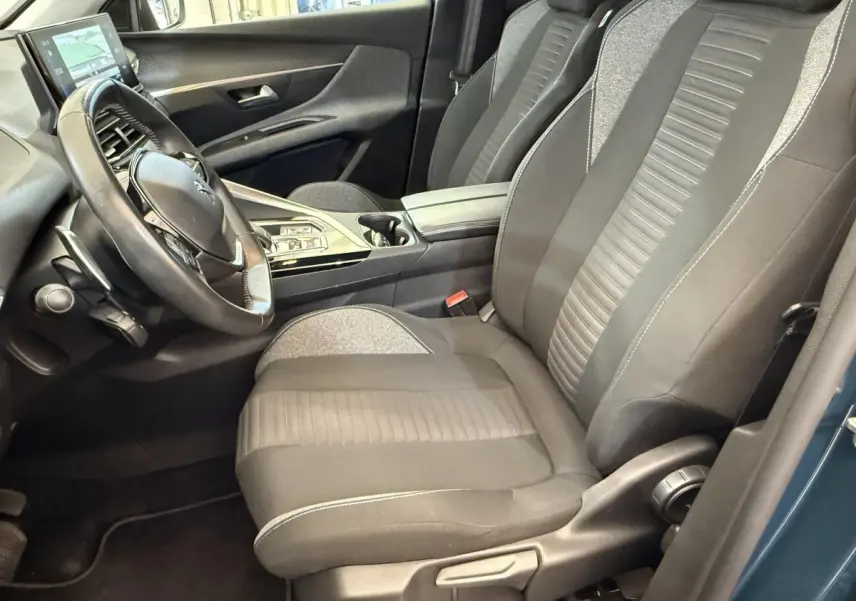 Vue intérieure côté conducteur du Peugeot 3008 bleu, montrant le volant cuir, sièges tissu bicolores et console centrale moderne.