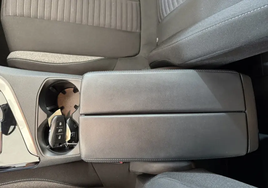 Vue rapprochée de l'accoudoir central noir et porte-gobelets avec clé de Peugeot 3008 bleu, intérieur tissu gris.