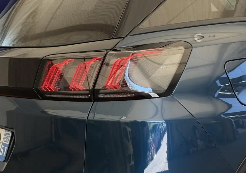 Gros plan sur le feu arrière droit rouge d’un Peugeot 3008 bleu, soulignant la ligne noire entre les feux.