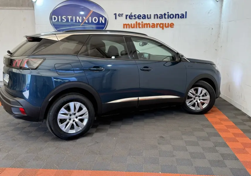 Vue latérale droite d’un Peugeot 3008 bleu 2021 avec jantes alliage et rails de toit assortis en intérieur showroom.