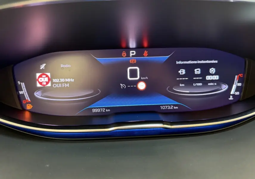 Affichage numérique du tableau de bord du Peugeot 3008 bleu, montrant la radio, vitesse à 0 km/h et jauges carburant et température.