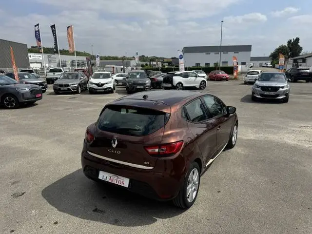 Renault Clio IV marron vue 3/4 arrière droit sur parking avec barres de toit et vitres surteintées.
