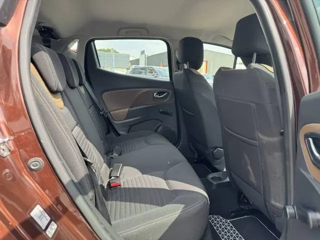 Vue intérieure côté gauche des sièges arrière d'une Renault Clio IV marron, montrant les sièges en tissu gris et la porte ouverte.