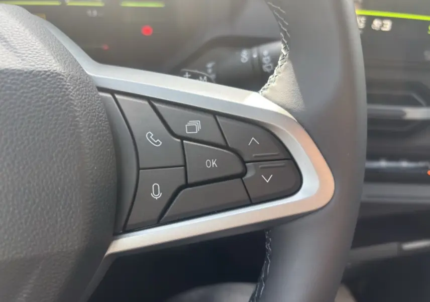 Gros plan sur les commandes au volant cuir du Dacia Bigster Hybrid-G 150, intérieur noir avec écran de bord flou en arrière-plan.