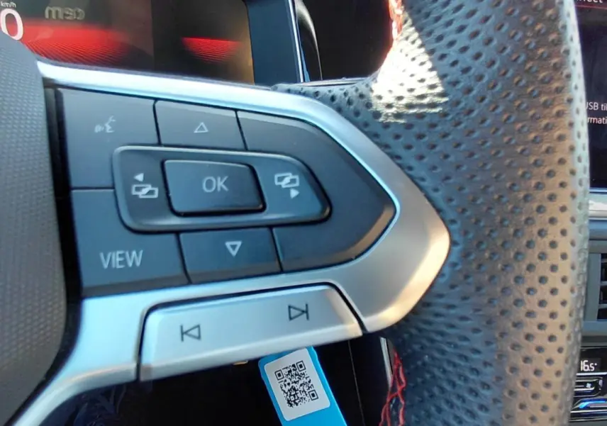 Gros plan sur le volant sport perforé de la Volkswagen Polo GTI 2024 avec commandes intégrées et cockpit numérique en arrière-plan.