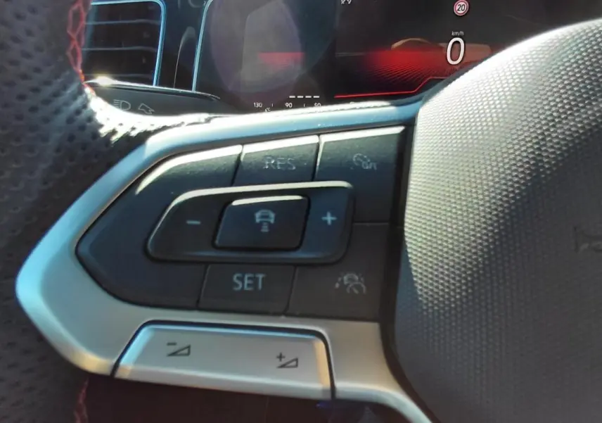 Gros plan sur les commandes du volant sport noir de la Volkswagen Polo GTI 2024 avec affichage numérique en arrière-plan.