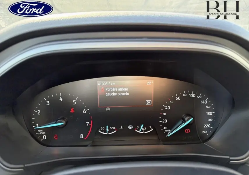 Vue rapprochée du tableau de bord de la Ford Focus bleu azur, affichant un message d'alerte porte arrière gauche ouverte.