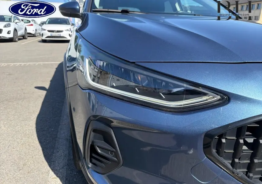 Gros plan sur l'avant gauche de la Ford Focus bleu azur métallisé, mettant en valeur le phare LED et la calandre noire.