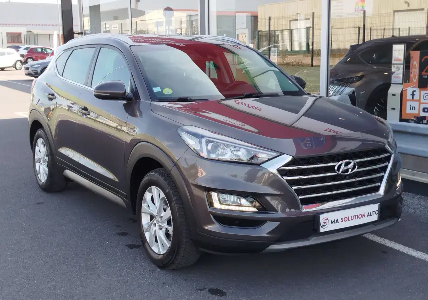 Vue 3/4 avant droit d'un Hyundai Tucson gris Micron 2019 avec calandre chromée et feux LED allumés.