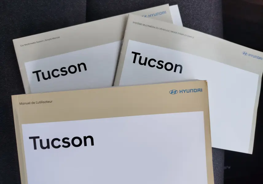 Image montrant trois manuels d'utilisation Hyundai Tucson posés en éventail sur un tissu sombre, sans véhicule visible.