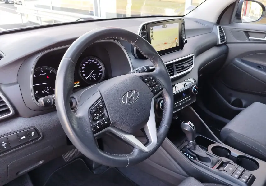 Vue intérieure côté conducteur du Hyundai Tucson 2019, tableau de bord gris avec écran tactile et volant cuir multifonctions.