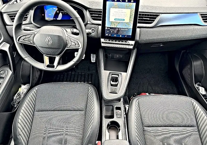 Vue intérieure avant de la Renault Symbioz 2026, tableau de bord noir avec écran tactile vertical et sièges en tissu noir.
