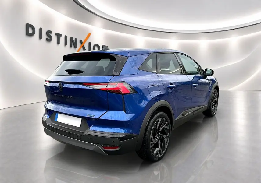 Vue 3/4 arrière droite du Renault Symbioz bleu iron avec jantes noires et feux arrière LED fins dans un showroom moderne.