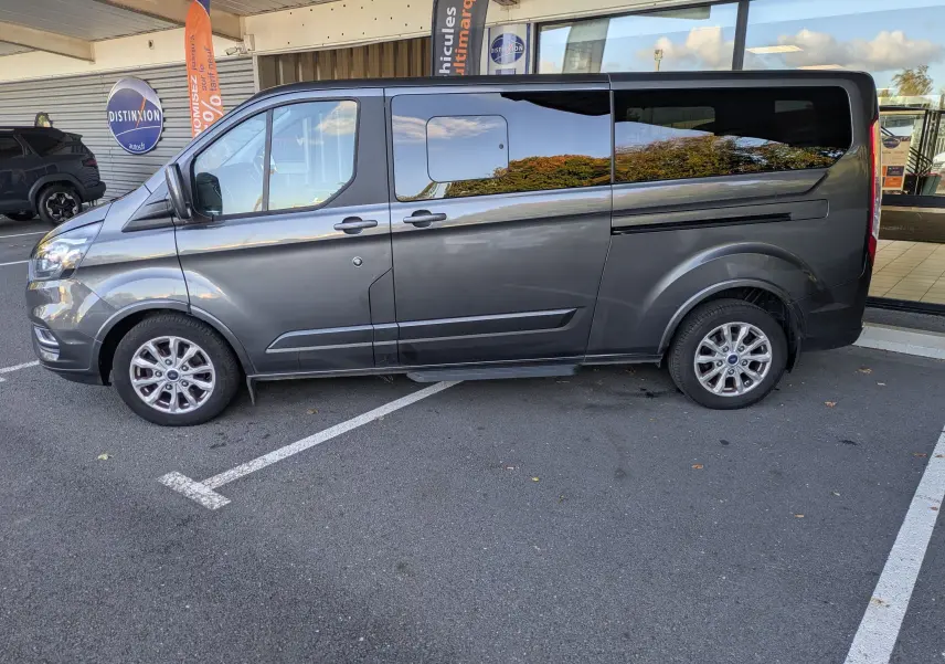 Vue de profil côté gauche d’un Ford Tourneo Custom gris 2019, grand van familial avec vitres teintées et jantes alliage.