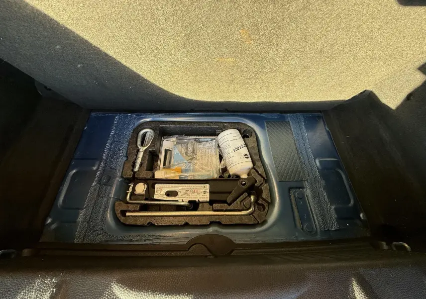 Coffre ouvert d'une MINI Cooper bleu 2007 montrant le kit de dépannage et les outils de bord.