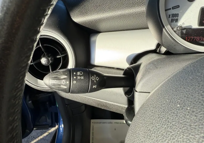 Gros plan sur le commodo gauche du tableau de bord d'une MINI Cooper bleu, avec aérateur circulaire visible.