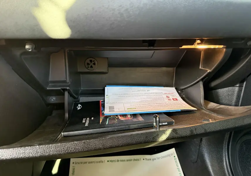 Gant de rangement ouvert côté passager d'une MINI Cooper bleu, avec documents et lumière intérieure allumée.