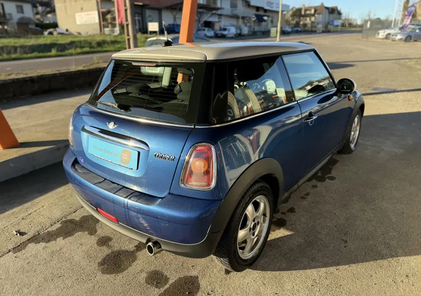 Vue 3/4 arrière droite d'une MINI Cooper 2007 bleu avec toit blanc et jantes alliage 15 pouces.