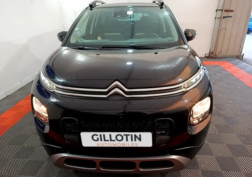Citroën C3 Aircross noir vue de face en intérieur, avec phares allumés et barres de toit visibles.