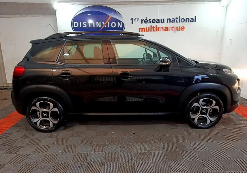 Profil côté gauche d'un Citroën C3 Aircross noir 2019 avec barres de toit et jantes distinctives en intérieur showroom.