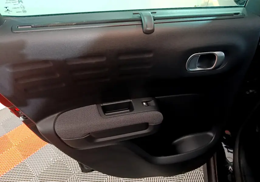 Gros plan sur la porte intérieure côté gauche du Citroën C3 Aircross noir, avec poignée argentée et accoudoir tissu.