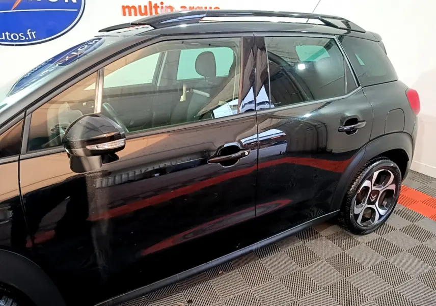 Profil côté gauche d'un Citroën C3 Aircross noir 2019 avec barres de toit et jantes distinctives en intérieur showroom.