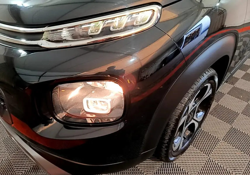 Gros plan sur le phare avant droit allumé d'un Citroën C3 Aircross noir, avec jante alliage et carrosserie brillante.