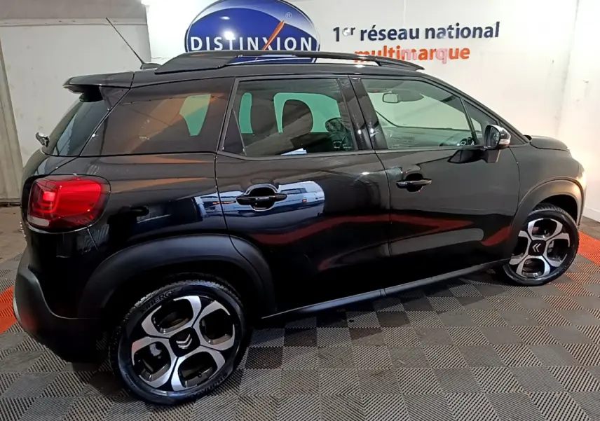 Profil côté droit d'un Citroën C3 Aircross noir 2019 avec barres de toit et jantes distinctives en intérieur showroom.