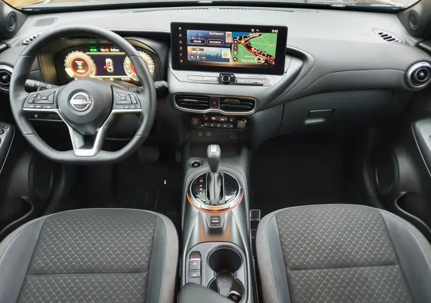 Vue intérieure avant du Nissan Juke 2025 noire, avec tableau de bord numérique et écran tactile central affichant la navigation.