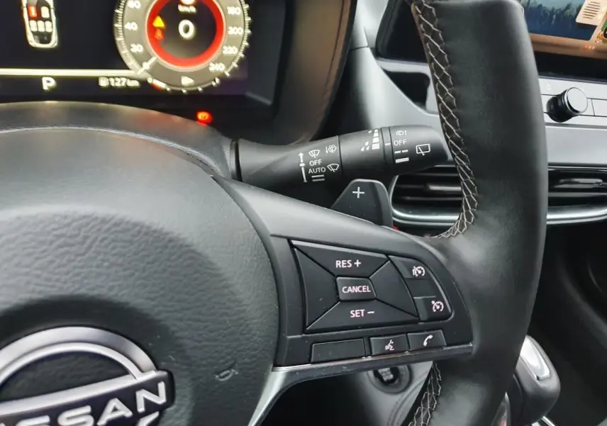 Gros plan sur le volant cuir noir du Nissan Juke 2025 avec commandes de régulateur et tableau de bord numérique.