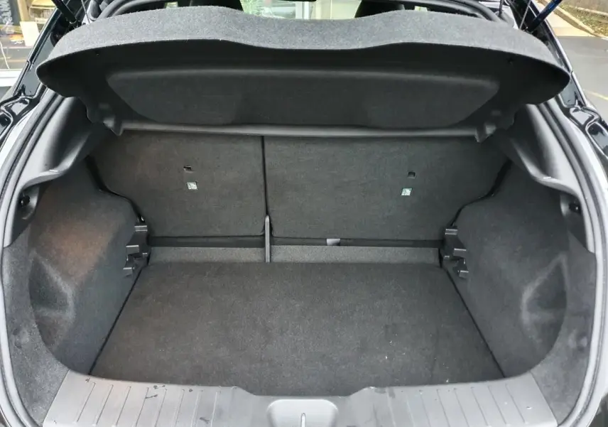 Coffre ouvert vu de l'arrière d'un Nissan Juke noir 2025, montrant l'espace de chargement vide et la banquette rabattable.