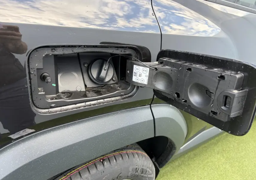 Gros plan sur la trappe de carburant ouverte côté gauche du Dacia Bigster noir nacré avec jante 18 pouces visible.