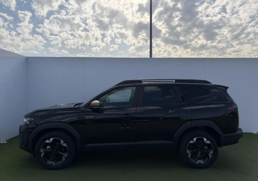 Profil côté gauche du Dacia Bigster noir nacré 2025 avec jantes alliage et rétroviseurs brun cuivré sous ciel nuageux.