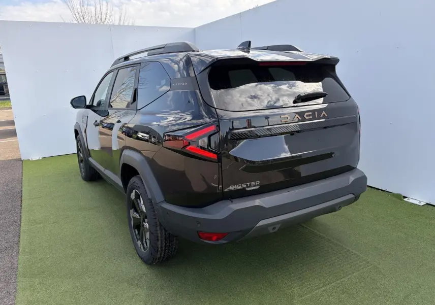 Vue 3/4 arrière gauche du Dacia Bigster noir nacré avec signature lumineuse LED et barres de toit noires.