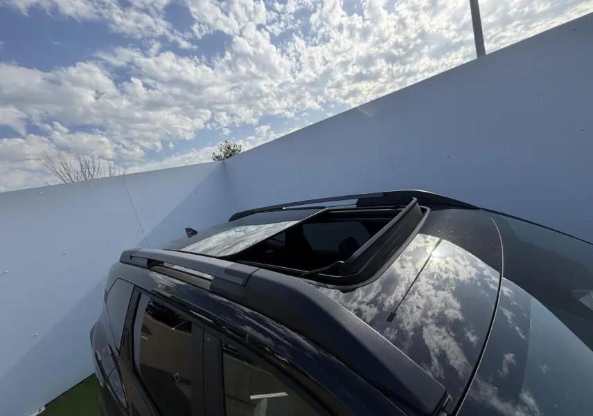 Toit ouvrant panoramique ouvert sur le côté gauche d’un Dacia Bigster noir nacré avec barres de toit noires.