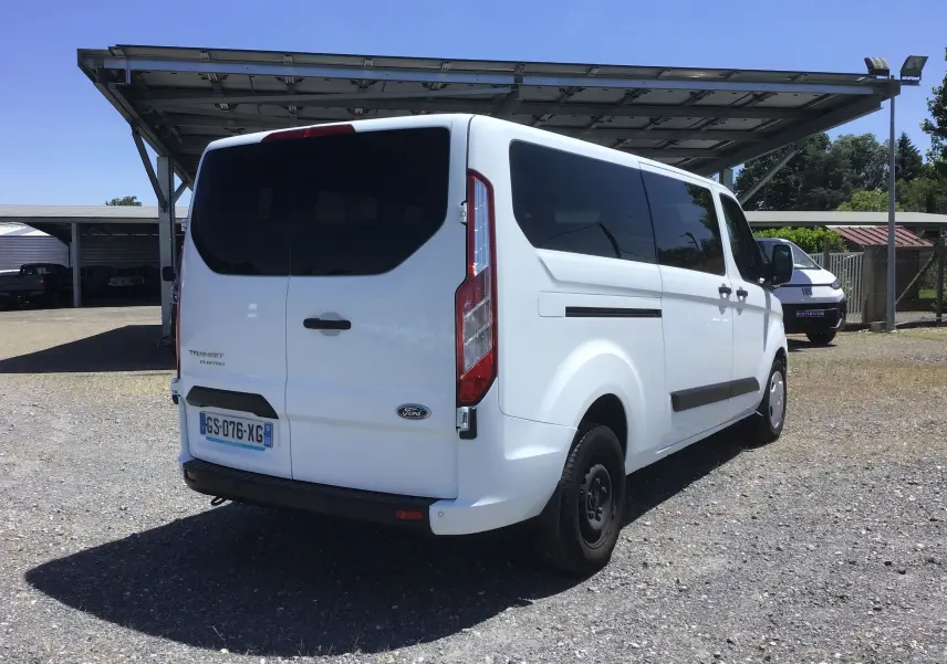 Vue 3/4 arrière droite d’un Ford Transit Custom Kombi blanc 2023 avec vitres teintées et porte arrière double.