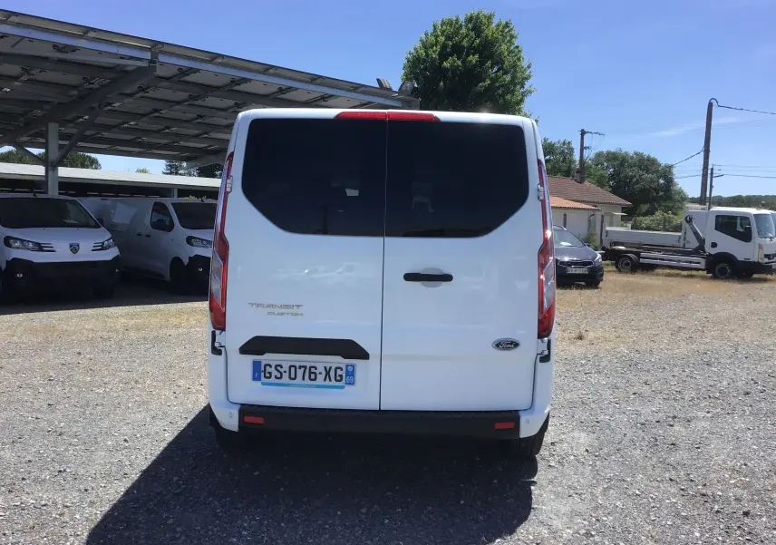 Vue arrière d'un Ford Transit Custom Kombi blanc 2023, avec portes battantes fermées et vitres arrière teintées.