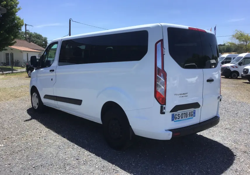 Vue 3/4 arrière droite d’un Ford Transit Custom Kombi blanc, avec vitres arrière teintées et hayon fermé.