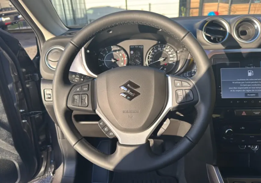 Vue intérieure centrée sur le volant cuir noir du Suzuki Vitara 2025, avec tableau de bord et écran multimédia visible.