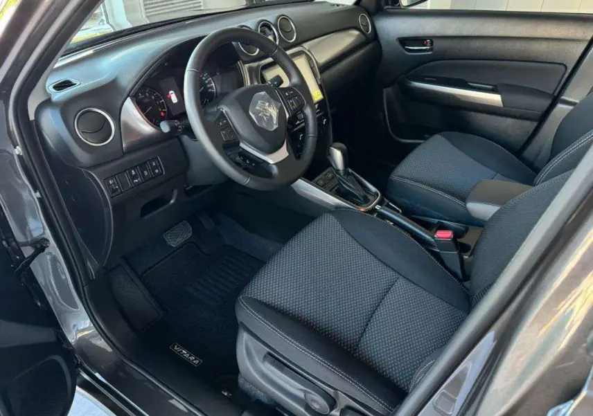 Vue intérieure côté conducteur du Suzuki Vitara 2025 gris Titan, avec volant cuir multifonctions et écran tactile central.