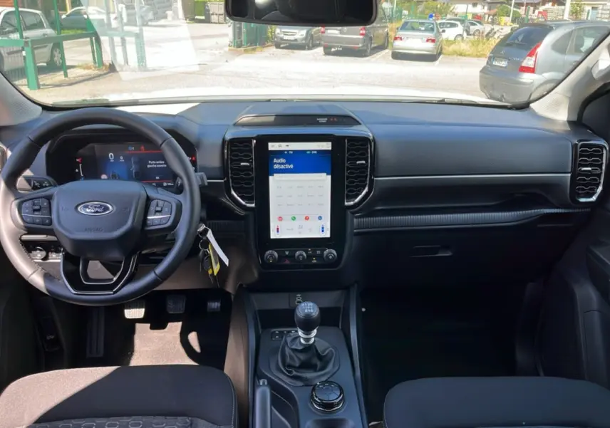 Vue intérieure avant du Ford Ranger 2026 blanc glacier, tableau de bord moderne avec écran tactile vertical et volant multifonctions.