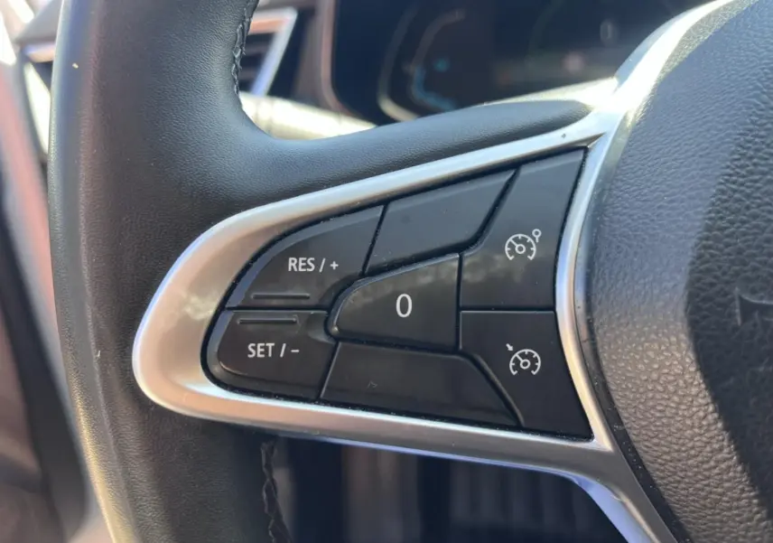 Gros plan sur les commandes de régulateur de vitesse au volant noir de la Renault Clio Blanc Quartz 2021.