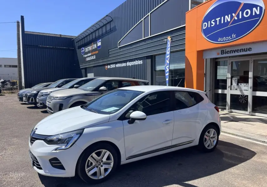 Vue 3/4 avant droite d'une Renault Clio blanc quartz garée devant un showroom avec enseigne orange Distinxion.